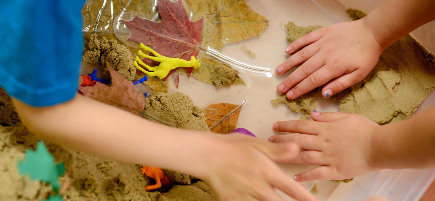 Children's hand playing with sand and pressed leaves