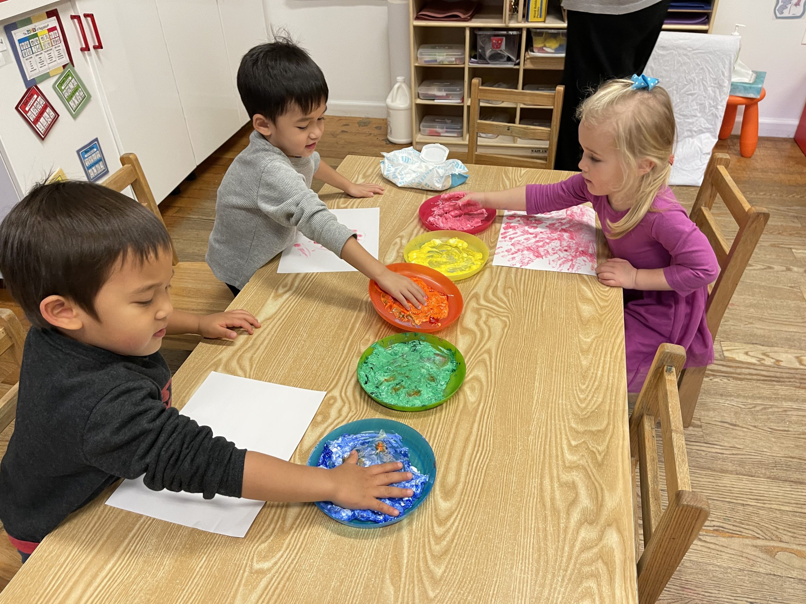 Children dipping their hands in color paint to make finger paintings